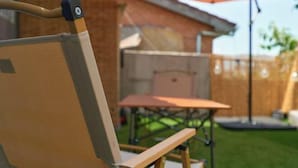 An outdoor patio area with a wooden table and chairs, a swing set, and a wooden fence.