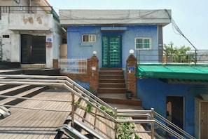A residential building with a blue facade, a green door, and a staircase leading to the entrance.