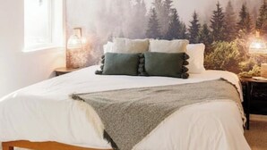 A bedroom with a bed, pillows, a blanket, a nightstand, a lamp, and a window. - Charming three bedroom near Glacier National Park (Columbia Falls)
