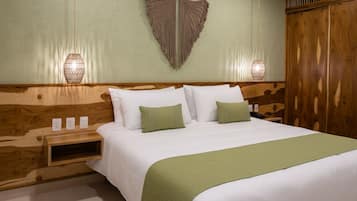 A neatly made bed with white linens and a green throw blanket, a wooden headboard, bedside lamps, and a wall-mounted macrame piece.