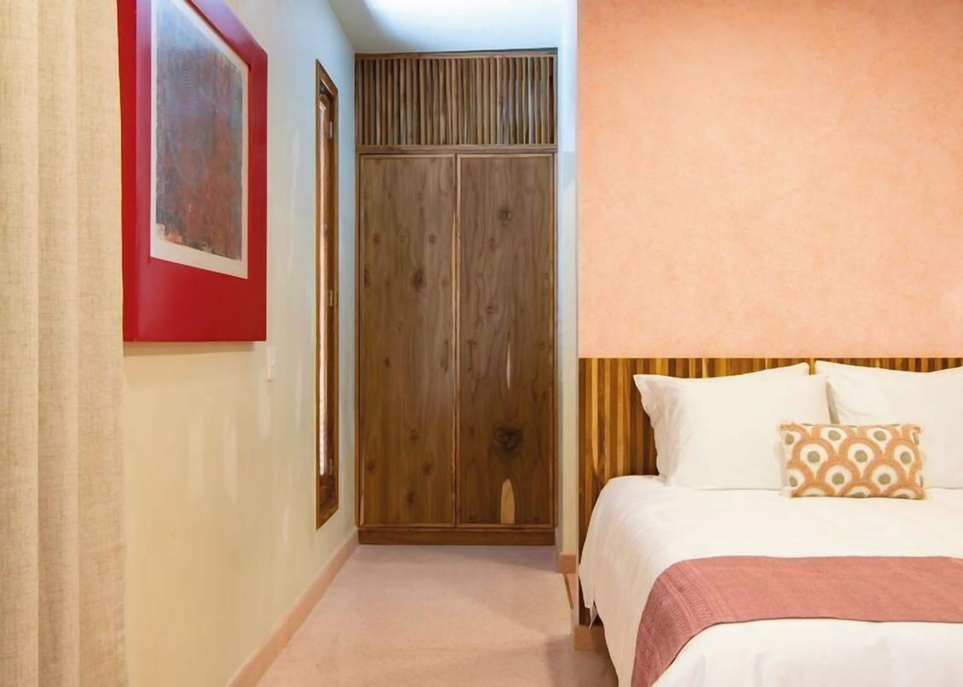 Une chambre à coucher avec un lit, une armoire en bois, un cadre photo rouge et un coussin à motifs.