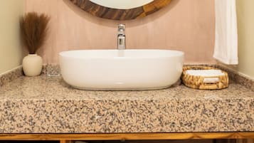 A bathroom with a round mirror, a white sink, a towel rack, and a shelf with folded towels.