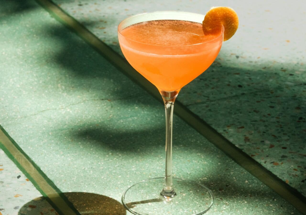 Un cóctel en una copa de martini con una guarnición sobre una superficie moteada.