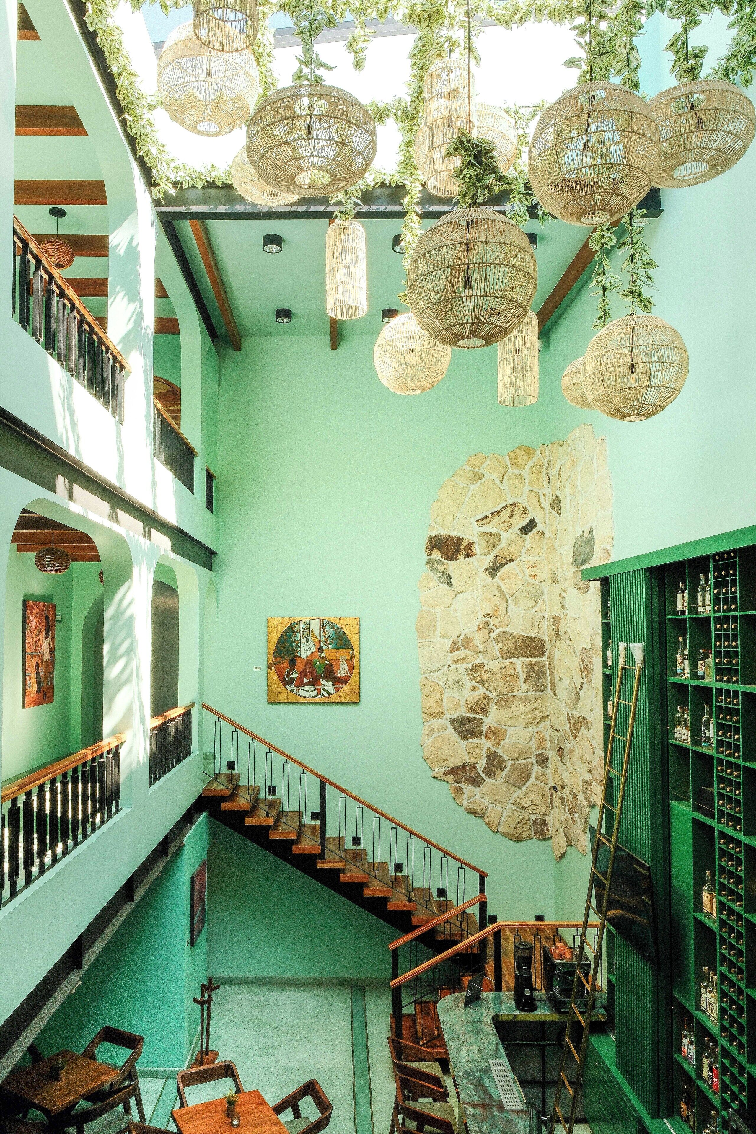 A multi-level interior with a staircase, wicker hanging lights, a stone wall, and a green bookshelf.