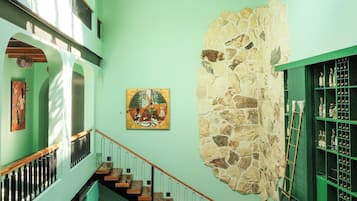 A multi-level interior with a staircase, wicker hanging lights, a stone wall, and a green bookshelf.