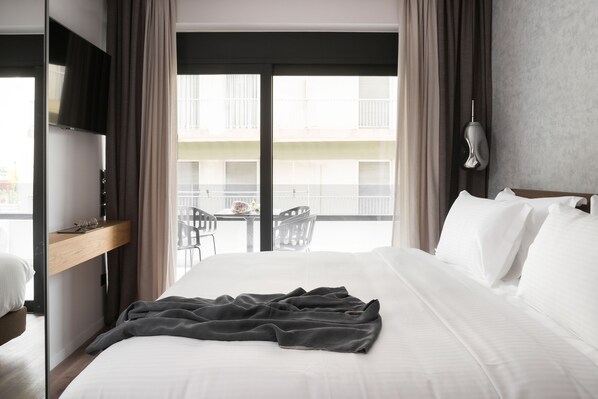 A hotel room with a bed, a TV, a balcony with chairs, and a view of buildings. - Lux&easy Athens Downtown Apartments (Athens)