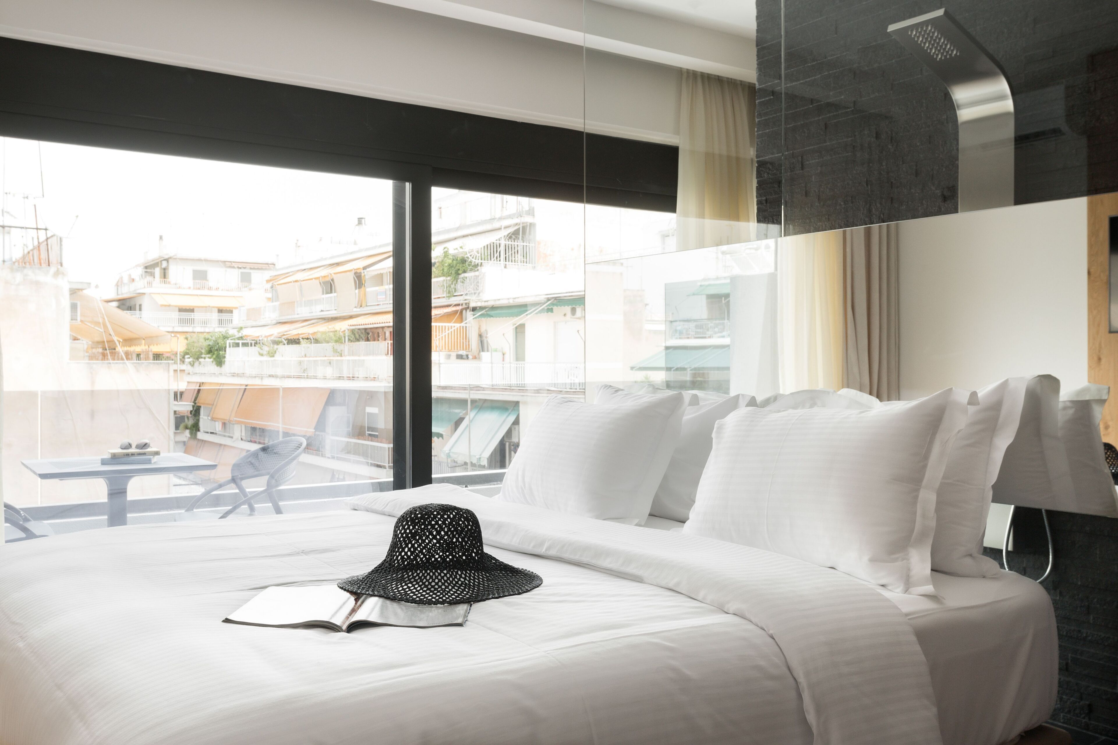 A hotel room with a large bed, a view of the city through floor-to-ceiling windows, and a balcony with outdoor furniture.