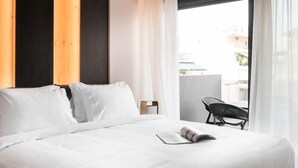A hotel room with a bed, a window with curtains, a chair, and a view of the outside. - Lux&easy Athens Downtown Apartments (Athens)