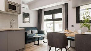 A modern kitchen with a microwave, a built-in oven, and a sink. There is a dining area with a table and chairs, and a sofa in the background. - Lux&easy Athens Downtown Apartments (Athens)