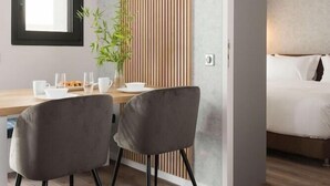 A modern hotel room with a wooden accent wall, a dining area with two chairs and a table, and a bed with white bedding. - Lux&easy Athens Downtown Apartments (Athens)