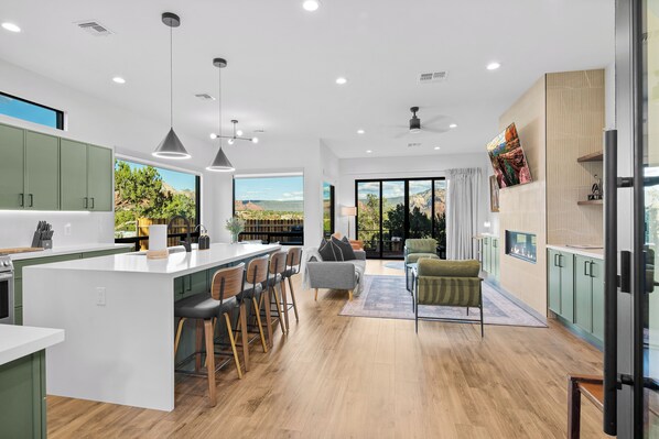 A modern kitchen with a large island, bar stools, and a view of a mountainous landscape.