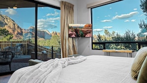 A bedroom with a large bed, a view of the mountains through a sliding glass door, and a balcony with outdoor furniture.