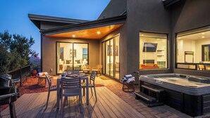 A modern outdoor patio with a hot tub, seating area, and a view of the interior.