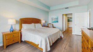 A bedroom with a wooden bed, two nightstands with lamps, a ceiling fan, and a door leading to another room. - Dog friendly bayfront 4th floor condo with bay views heated pool and spa WD (Clearwater)