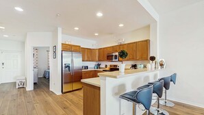 A modern kitchen with wooden cabinets, a stainless steel refrigerator, a microwave, and a bar area with stools. - Dog friendly bayfront 4th floor condo with bay views heated pool and spa WD (Clearwater)