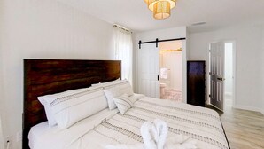 A bedroom with a large bed, a wooden headboard, and a hanging light fixture. - Bright and open home with private pool screened lanai enclosed yard and WD (Dunedin)