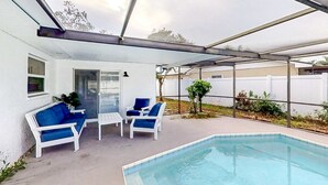 A covered outdoor area with a pool, white lounge chairs, and a glass door leading to a room. - Bright and open home with private pool screened lanai enclosed yard and WD (Dunedin)
