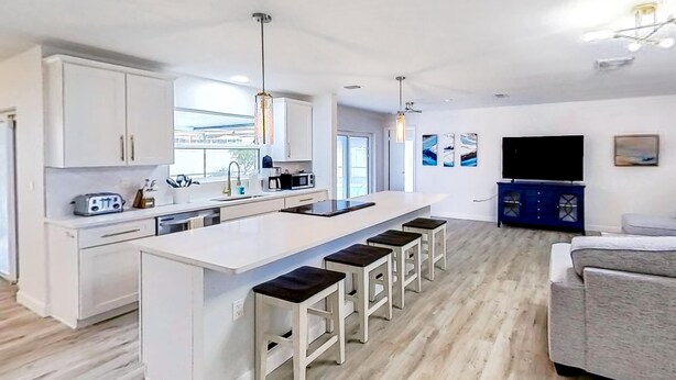 A modern kitchen with a central island, bar stools, and a dining area with a sofa. - Bright and open home with private pool screened lanai enclosed yard and WD (Dunedin)