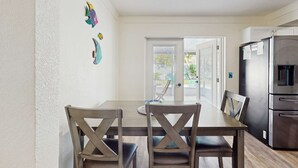 Un comedor con una mesa y sillas de madera, un refrigerador y una puerta que da a un espacio exterior.