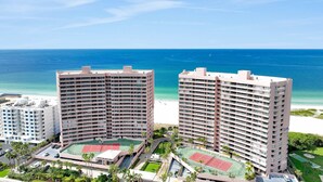 Ein Hochhaus-Hotel mit mehreren Etagen, einem Tennisplatz und Blick auf den Strand.