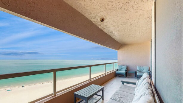 Ein Balkon mit Blick auf den Strand, eine Couch, ein kleiner Tisch und ein Stuhl.