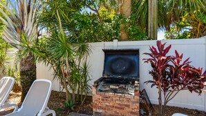 A patio with a brick grill, white lounge chairs, and various plants. - Beachside St Pete Condo w Heated Pool Near Landmark Restaurants (St. Pete Beach)