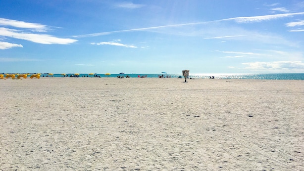 A wide sandy beach with umbrellas and a lifeguard tower. - Beachside St Pete Condo w Heated Pool Near Landmark Restaurants (St. Pete Beach)