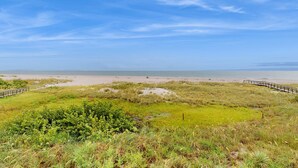 A coastal landscape with a sandy beach, grassy areas, and a wooden boardwalk. - 3rd floor beachfront condo with beach access pool Gulf views WD balcony AC (Treasure Island)