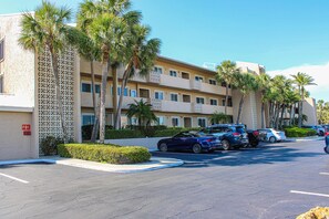 A multi-story hotel with a parking lot, palm trees, and a clear blue sky. - Chic and comfortable Gulf front condo snowbird and dog friendly pool beaches (Belleair Beach)