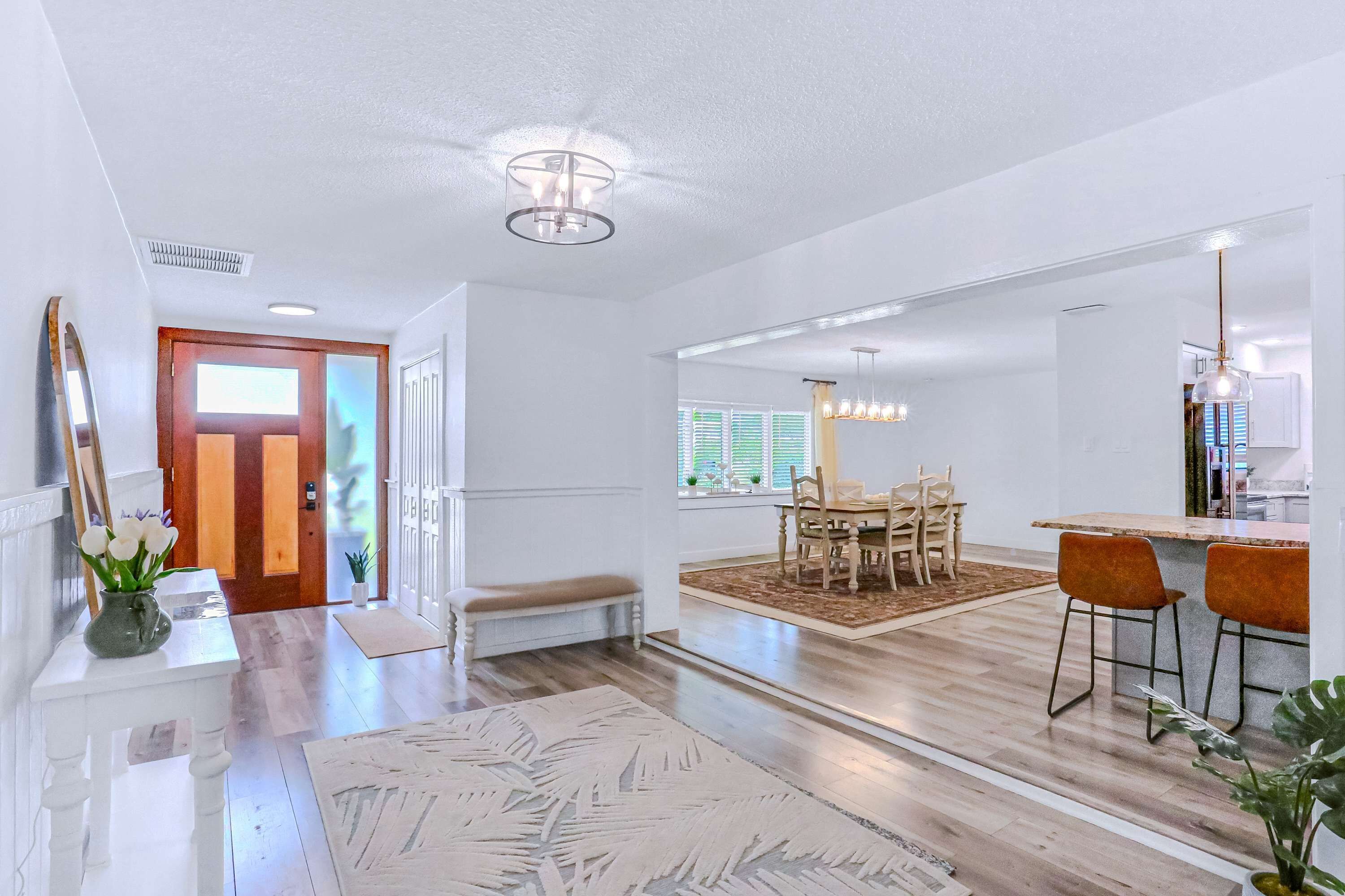 Un salón amplio con suelo de madera, una mesa de comedor con sillas, un banco y una zona de cocina con barra y taburetes.