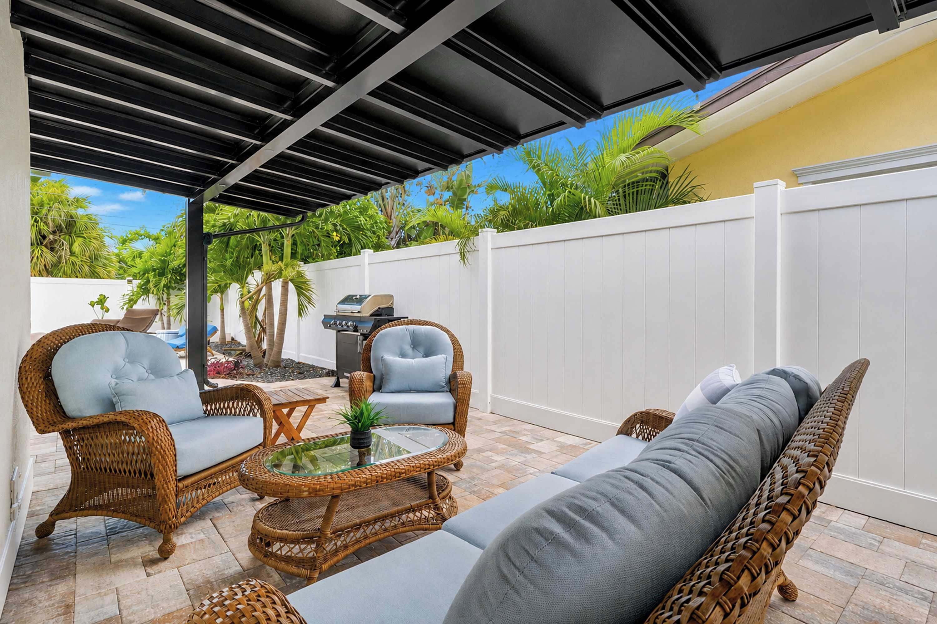 A covered patio area with wicker furniture, a glass-top table, and a grill.