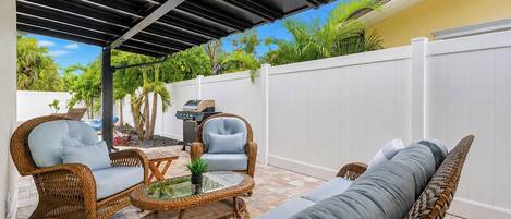 A covered patio area with wicker furniture, a glass-top table, and a grill.
