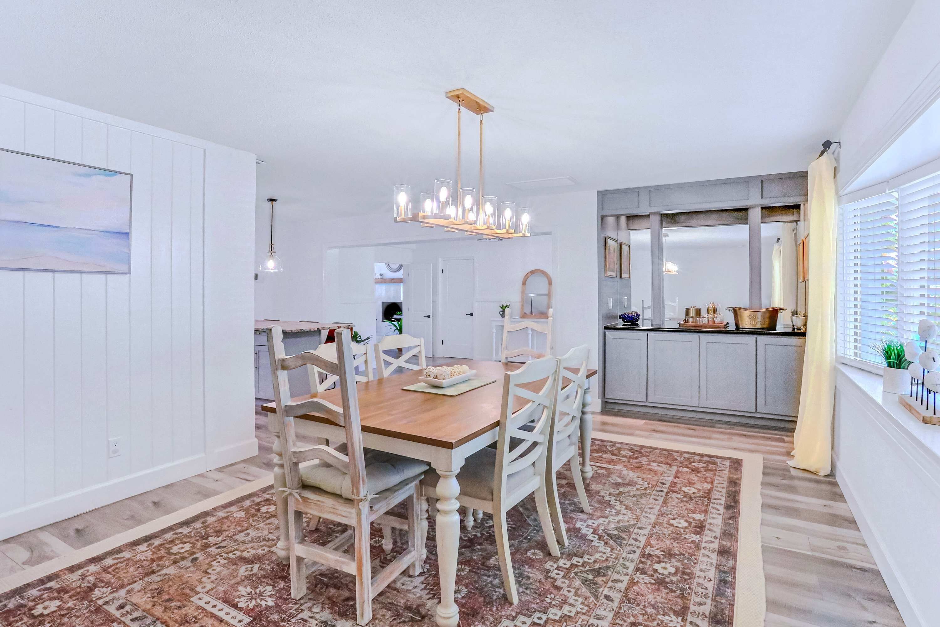 A dining area with a wooden table and chairs, a chandelier, and a patterned rug.