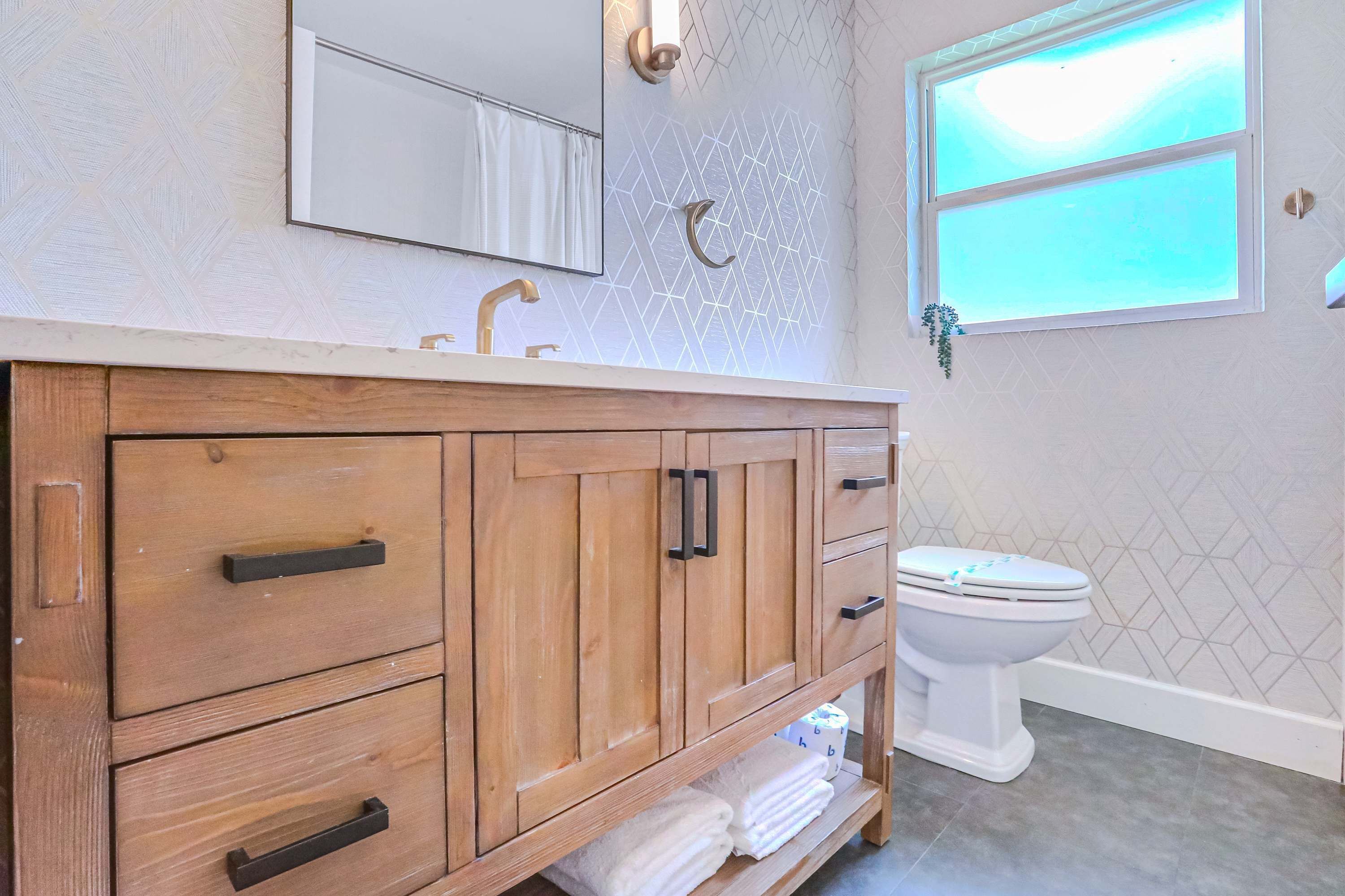 Un meuble-lavabo en bois, doté d’un miroir, d’un évier et de toilettes, dans une salle de bain aux murs décorés de motifs.