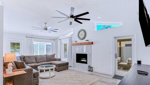 A modern living room with a grey sofa, a round coffee table, a fireplace, and a ceiling fan. - Large heated pool home with backyard oasis, AC and Wifi (Seminole)