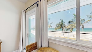 A room with a view of a beach, a wicker chair, and a wooden table.