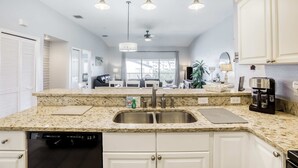 Una cocina moderna con encimeras de granito, armarios blancos, un lavamanos doble e iluminación colgante.