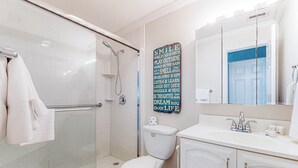 A bathroom with a glass shower enclosure, a white toilet, a sink with a mirror, and a motivational quote on the wall. - Centrally located condo with heated pool balcony washer dryer and central AC (Clearwater)