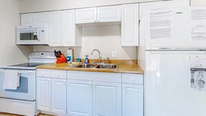 A kitchen with white cabinets, a microwave, a stove, a sink, and a refrigerator. There are papers on the refrigerator and a map on the wall. - Centrally located condo with heated pool balcony washer dryer and central AC (Clearwater)