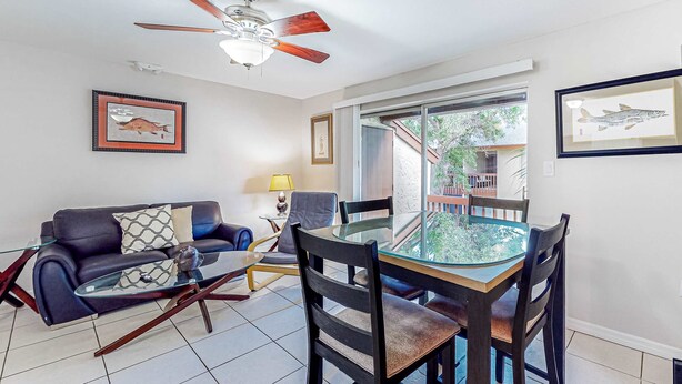 A living room with a glass-top dining table, dark wooden chairs, a black leather sofa, a ceiling fan, and framed fish artwork on the walls. - Centrally located condo with heated pool balcony washer dryer and central AC (Clearwater)