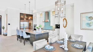 A modern kitchen with white cabinetry, a central island, pendant lighting, and a dining area with a wooden table and chairs.