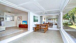 Amplia sala de estar con una mesa de comedor de madera, un televisor y una cocina visible al fondo.