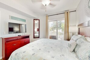 A bedroom with a bed, a dresser, a television, a mirror, and a balcony with curtains. - Second floor condo with beach access balcony pool hot tubs and ping pong (Treasure Island)