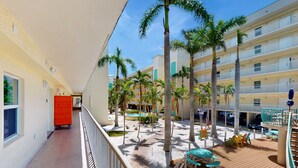 Pasillo de hotel con zona de piscina, palmeras y mobiliario exterior.