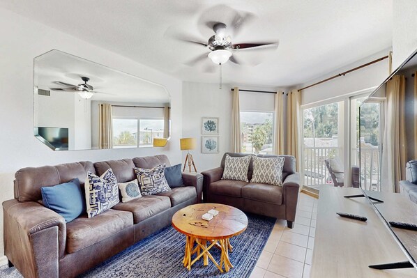 A spacious living room with two brown leather sofas, a round wooden coffee table, and a ceiling fan. - Second floor condo with beach access balcony pool hot tubs and ping pong (Treasure Island)