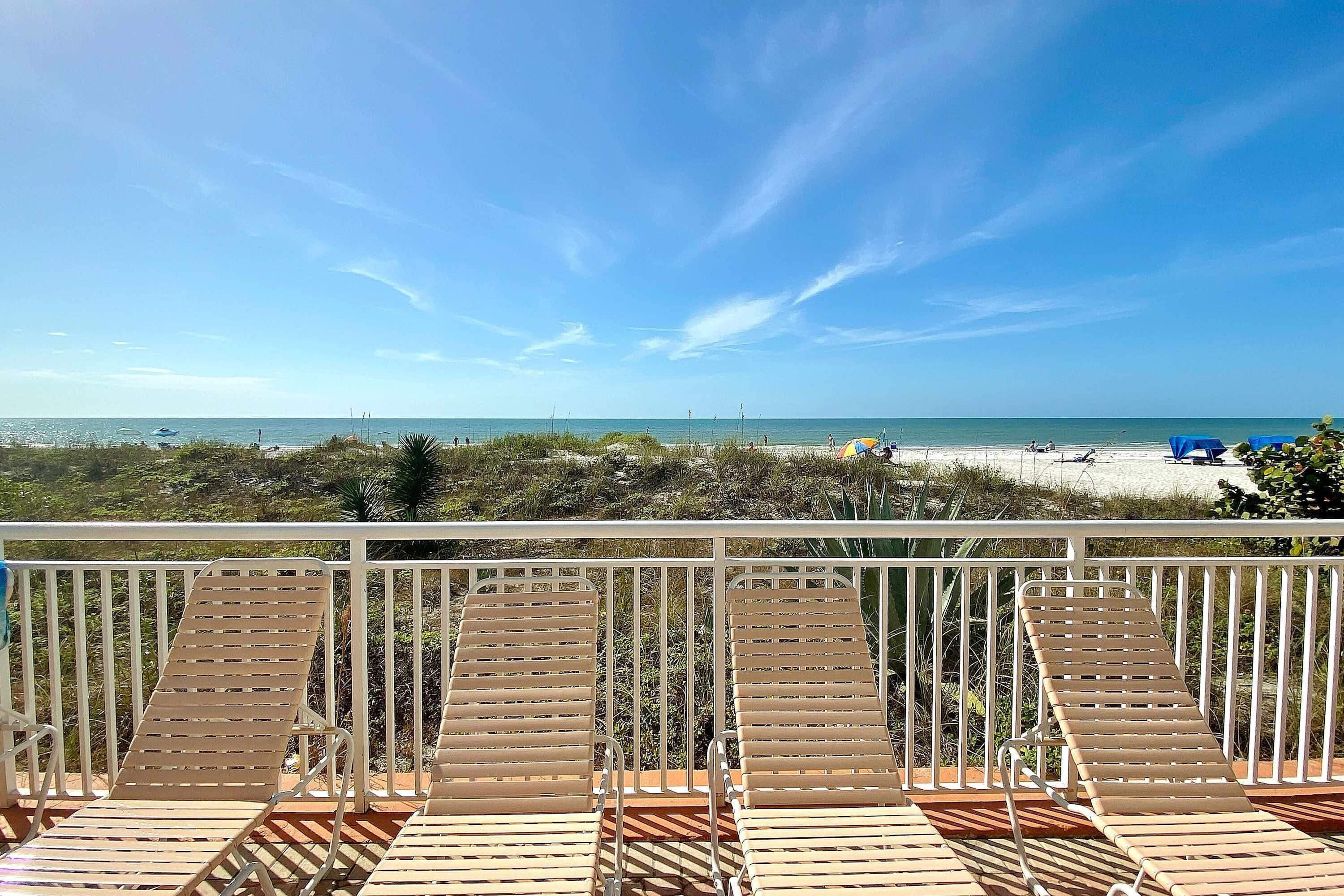 A balcony with wooden lounge chairs overlooking a beach.