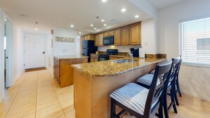 Una cocina moderna con encimeras de granito, armarios de madera, microondas integrado y una isla grande con taburetes de bar.