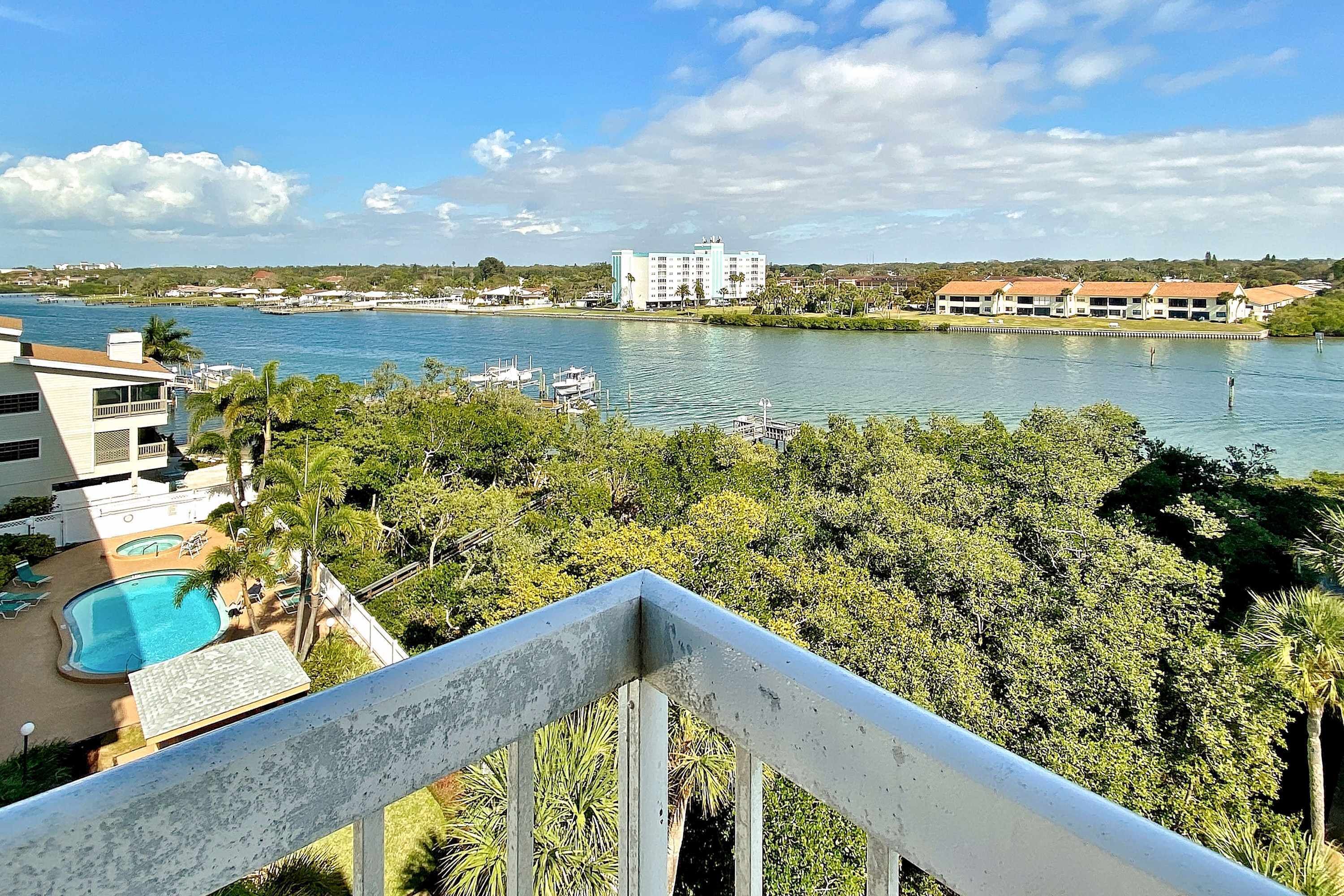 A hotel with a pool, a view of the water, and a distant building.