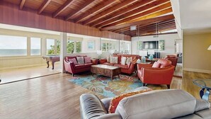 Amplia sala de estar con techo alto, vigas de madera, mesa de billar y un ventanal con vistas al exterior.