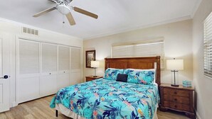 Un dormitorio con cama, ventilador de techo, lámparas de noche y una ventana con persianas.